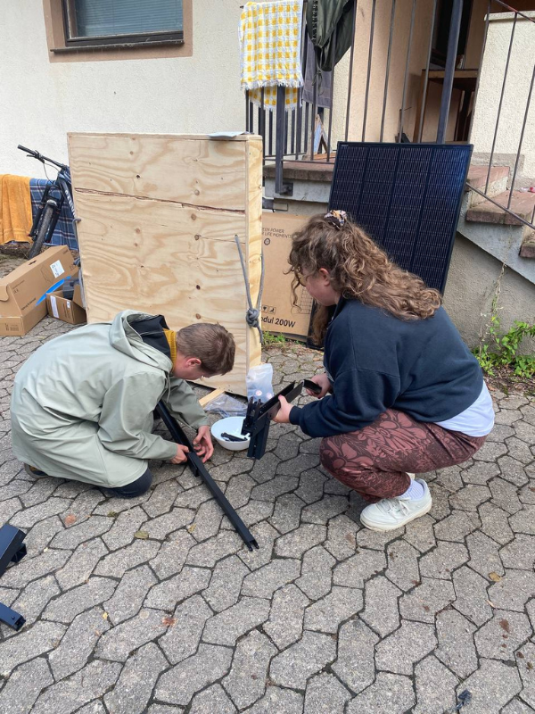 Zwei BalkonScouts sitzen in der Hocke und bauen ein Metallgestell zusammen.