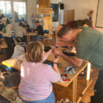 Der Workshopleiter des Balkonsolar-Workshops hilft einer Teilnehmerin beim Umbauen eines Kabelanschlusses.